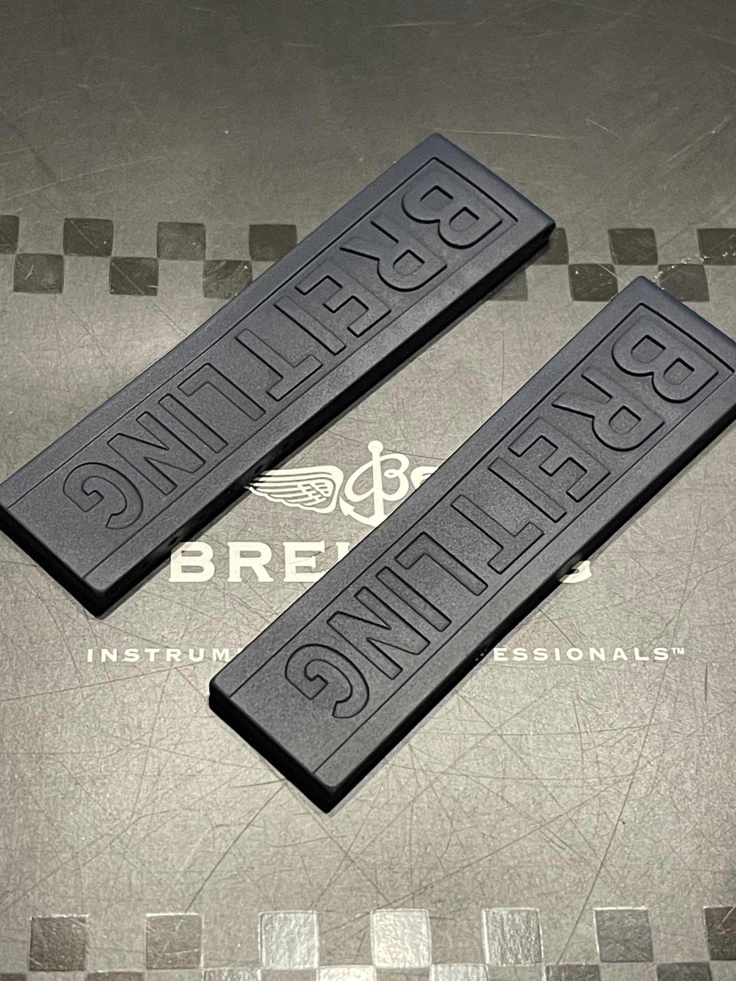 Two black racing-style Breitling Diver watch straps with 'BREITLING' embossed, displayed on a textured background with branding