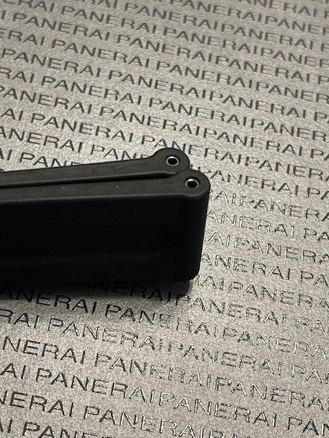 Black rubber strap component with two holes resting on Panerai logo textured background