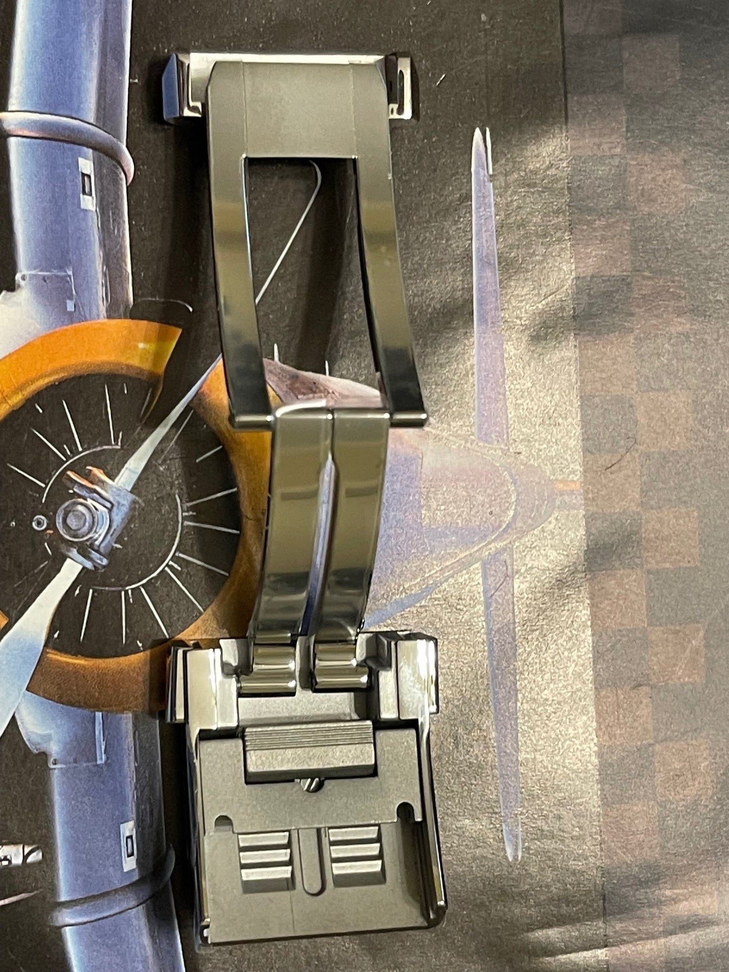 Breitling watch clasp in polished metal displayed over aviation-themed textured surface