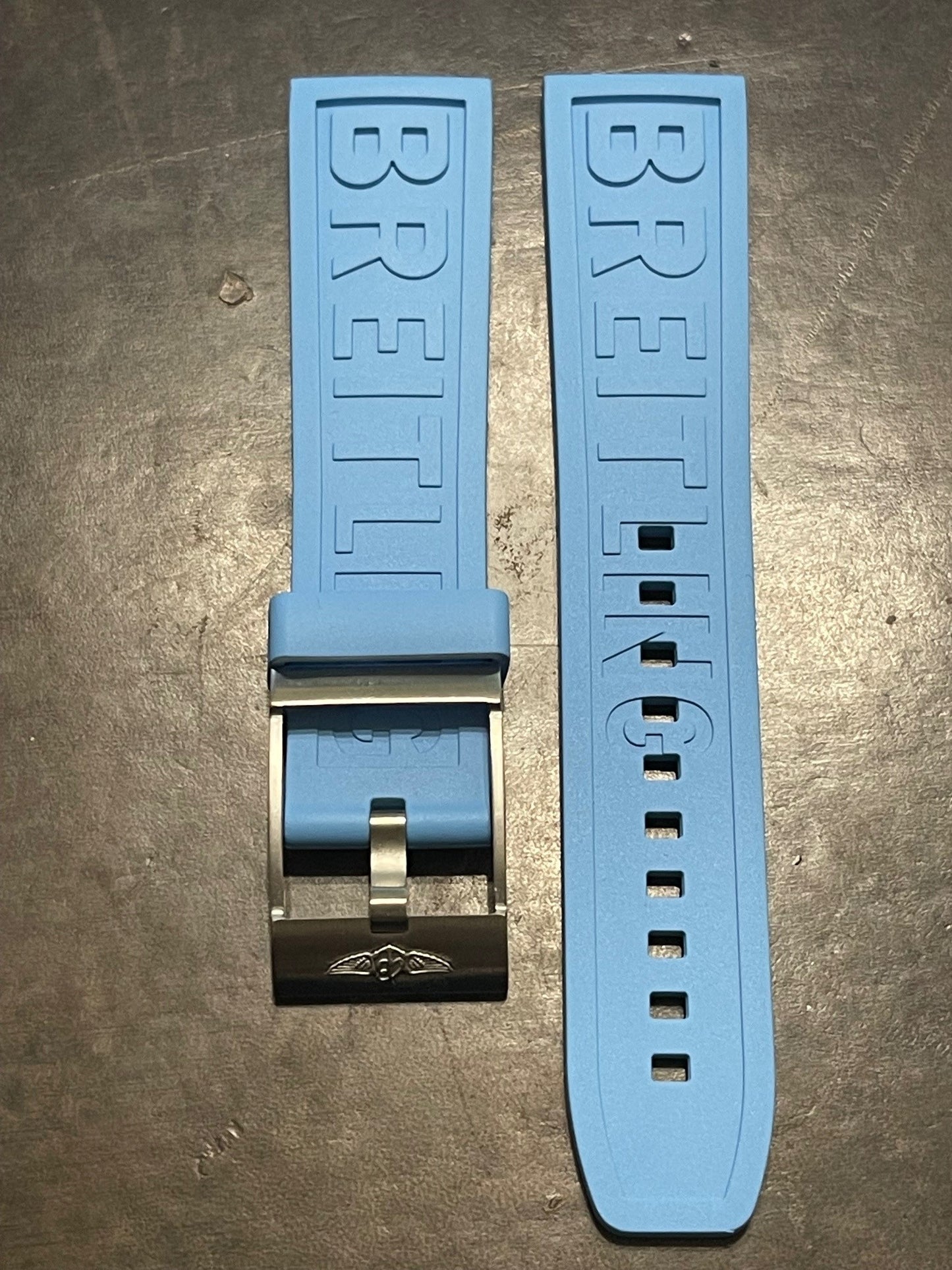Breitling light blue silicone watch strap with logo and metal buckle on dark background