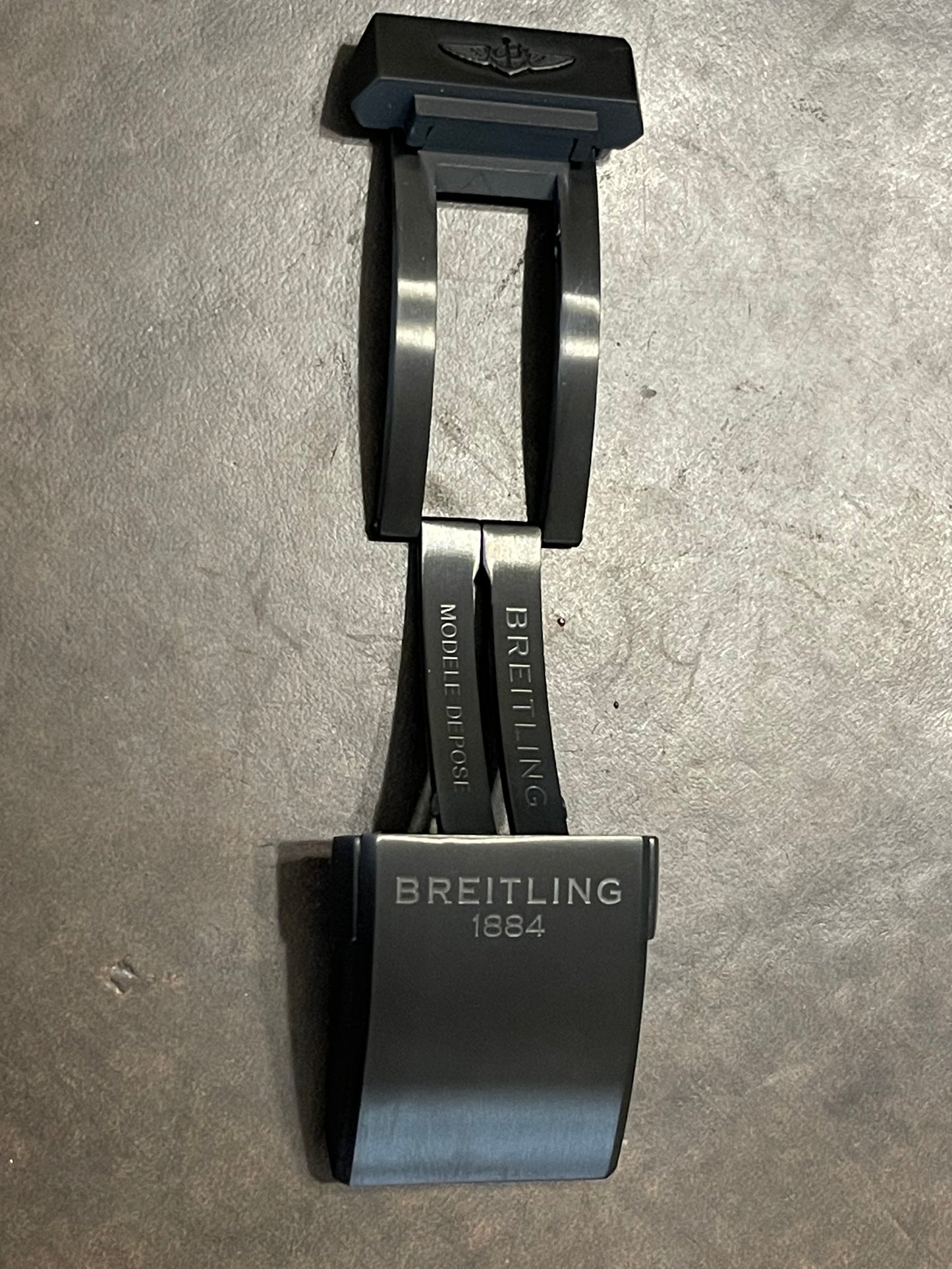 Breitling watch clasp in black with engraved text, shown on dark textured background
