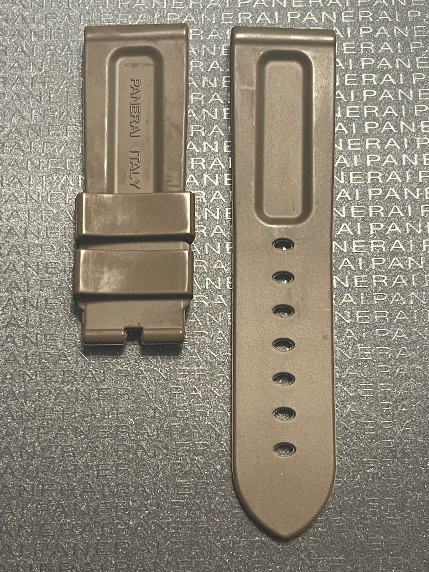 Close-up of a shiny Panerai watch buckle resting on a textured background featuring the Panerai logo.
