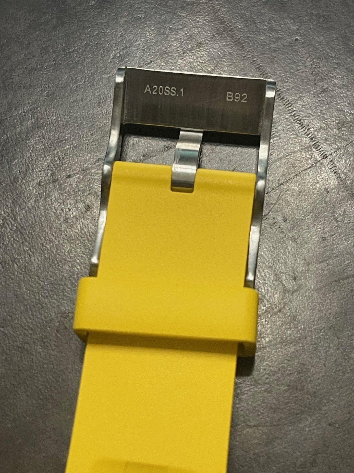 Breitling watch strap in yellow featuring silver buckle with engraved code on dark surface