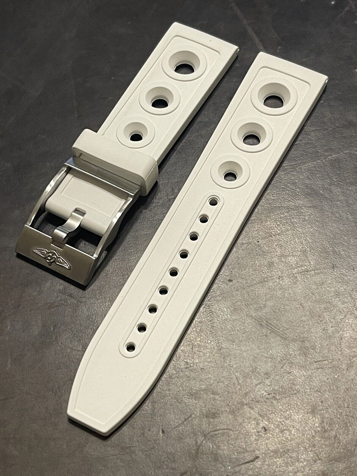 White watch strap and silver buckle on dark surface