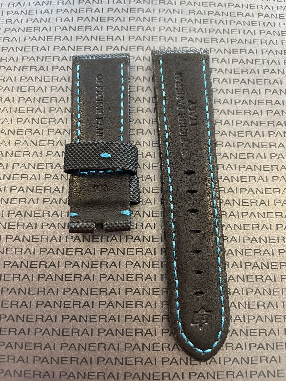 Panerai black leather watch strap with blue stitching on logo backdrop