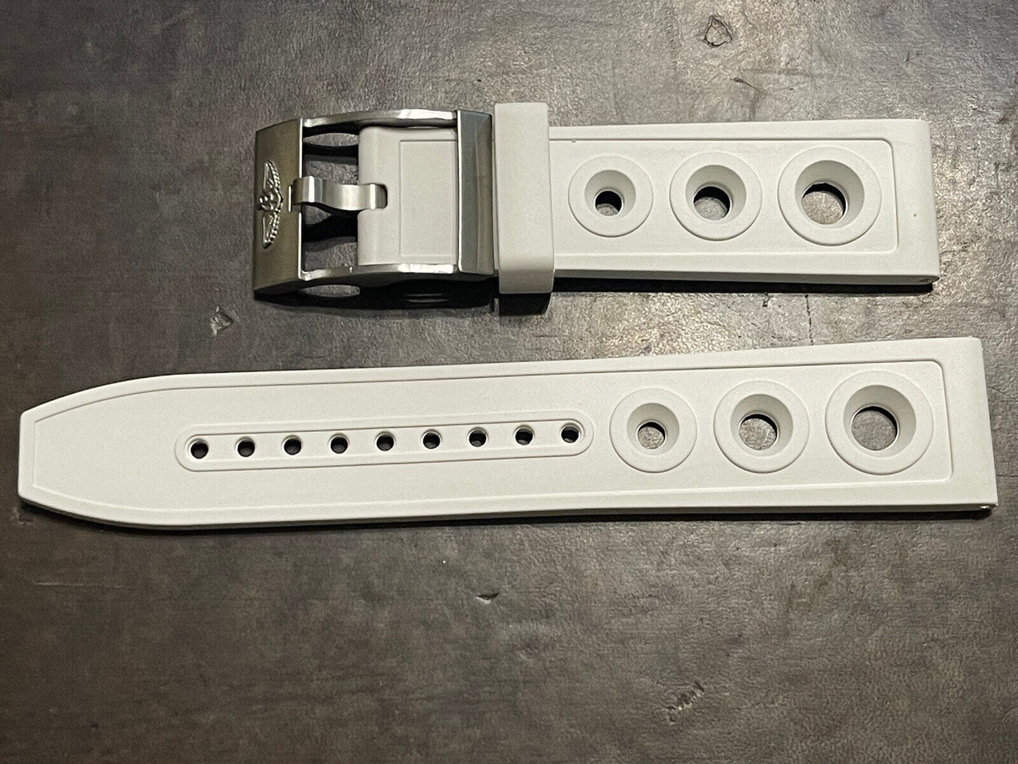 White rubber watch strap with silver buckle and adjustable holes on dark surface