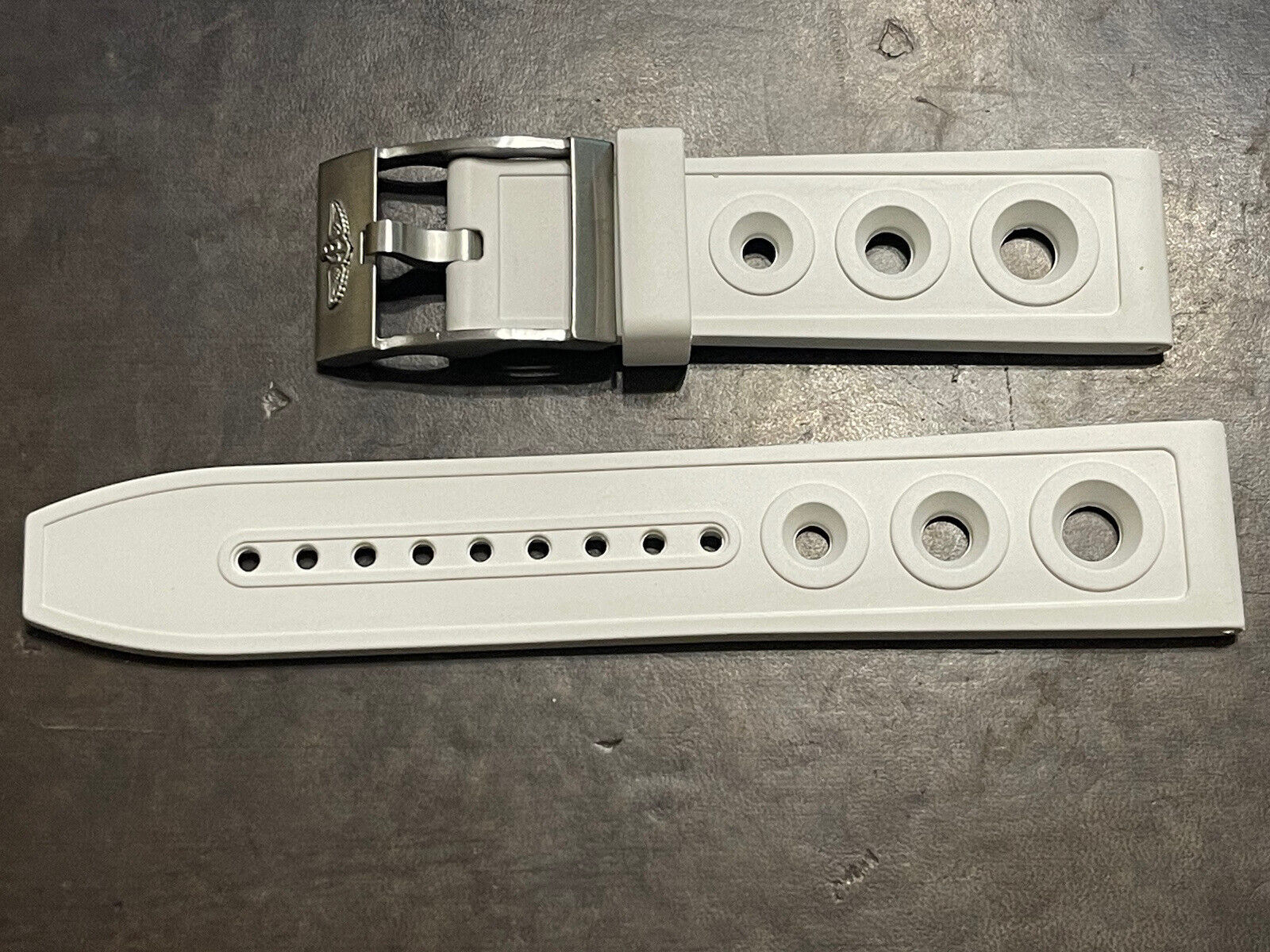 White rubber watch strap with silver buckle and adjustable holes on dark surface