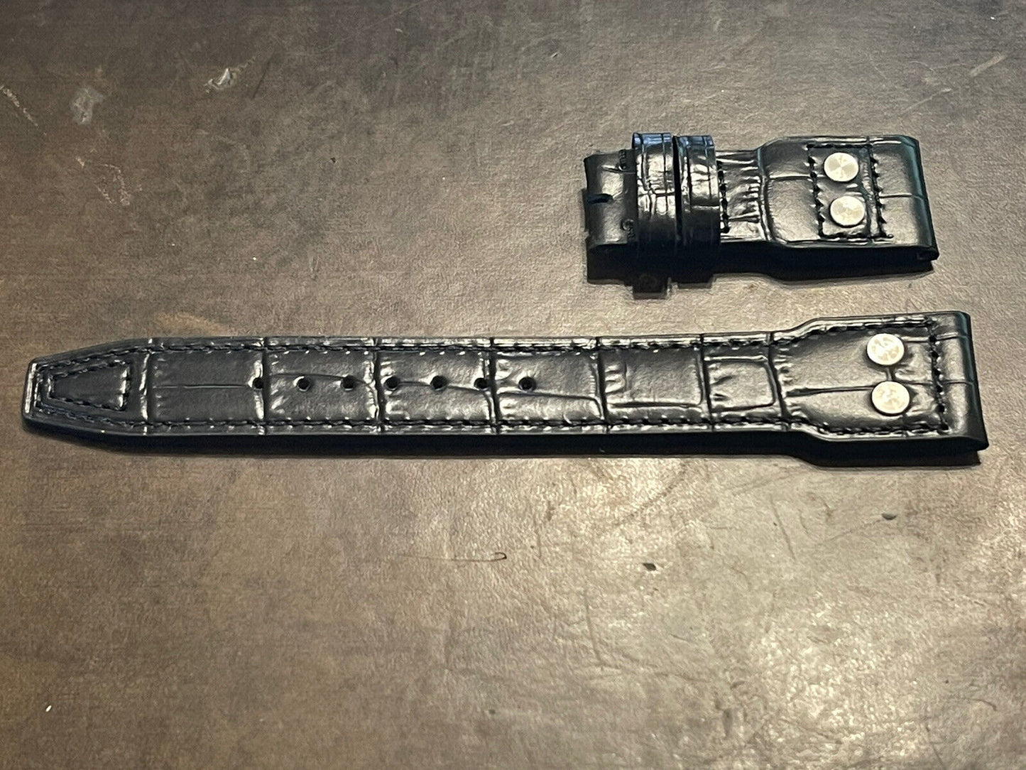 Two black leather watch straps with crocodile texture and metal details on dark surface