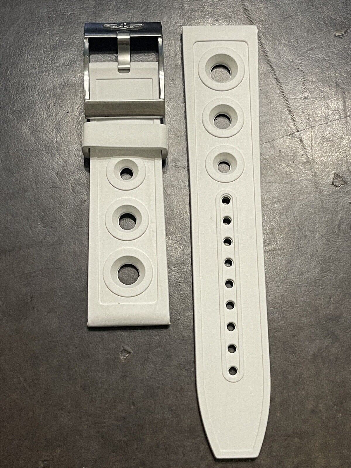 White rubber watch strap featuring buckle and fit holes, laid on dark surface