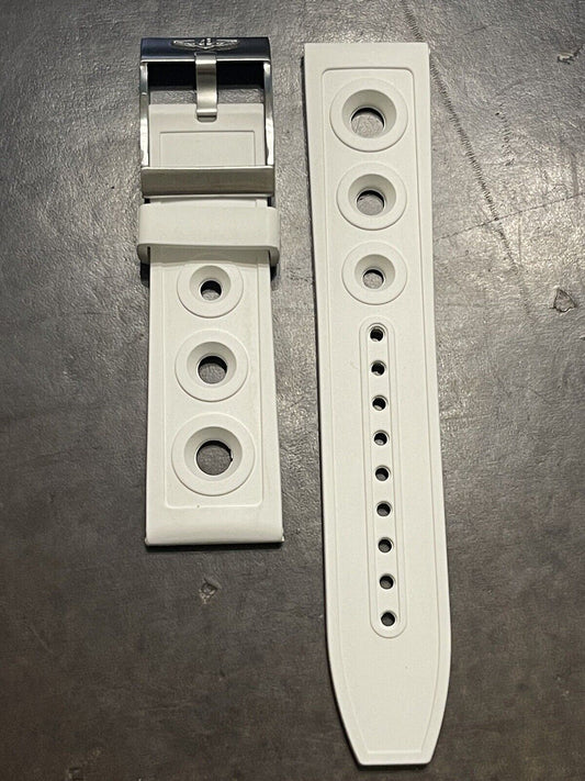 White rubber watch strap featuring buckle and fit holes, laid on dark surface