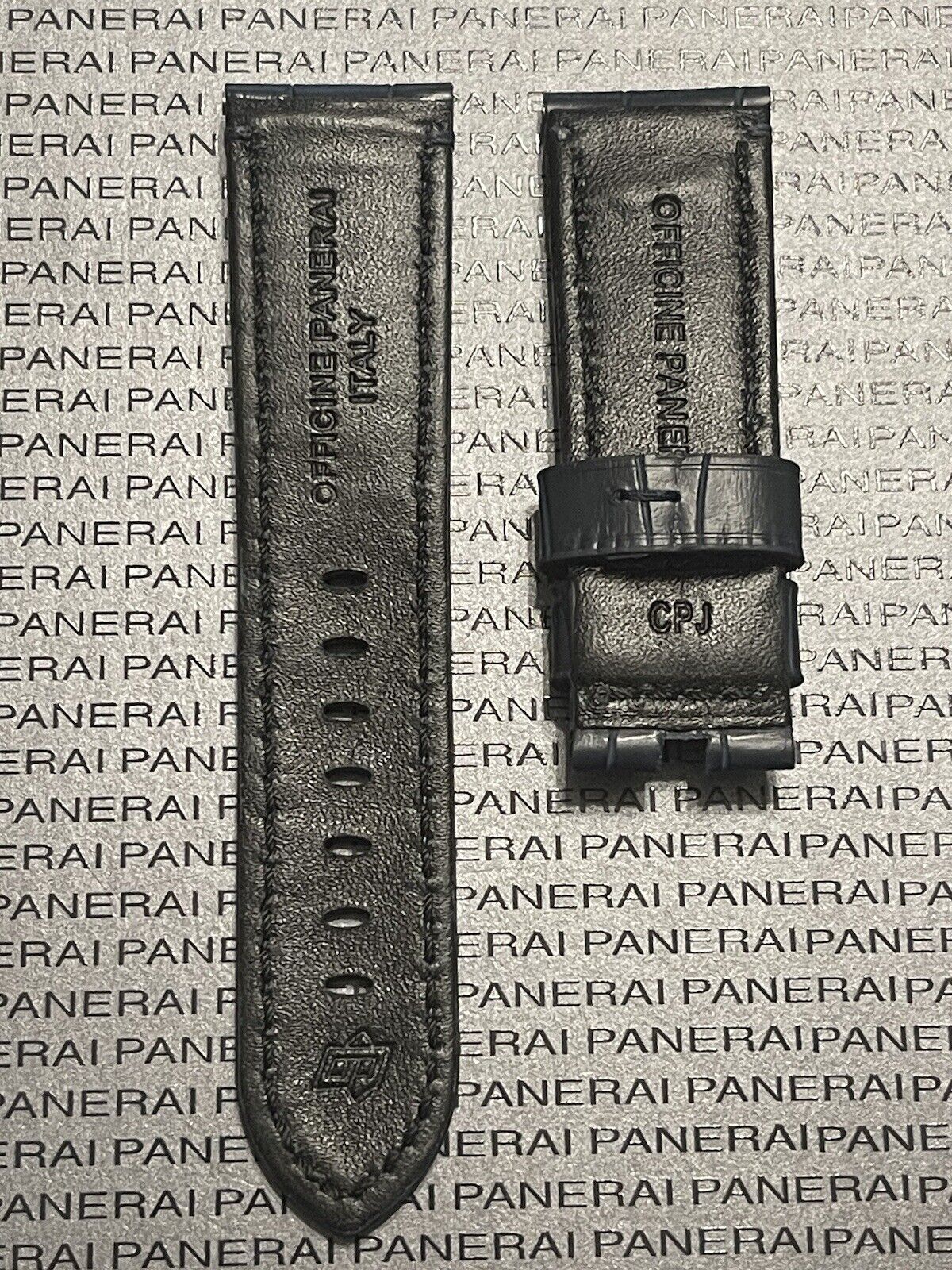 Two black Panerai watch straps on textured background with logo