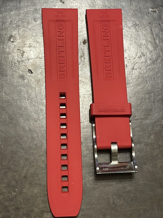 Breitling red rubber strap laid flat with metal buckle on rough background