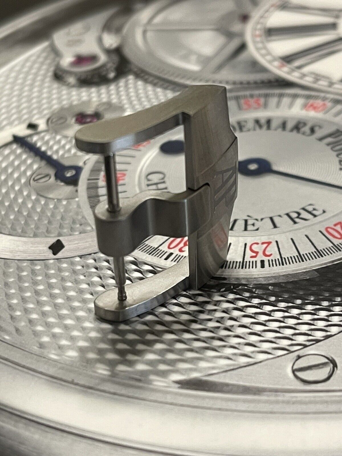 Close-up of luxury watch dial with precision components and metal lever on textured surface
