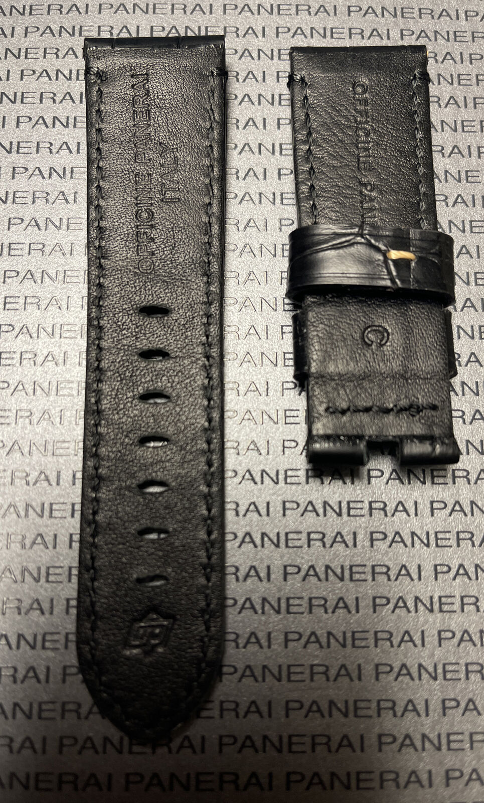 Close-up of black leather watch strap split in two with embossed branding on Panerai logo background