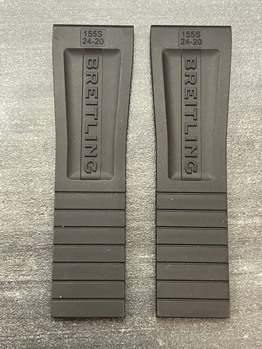 Two black rubber watch straps laid out on a wooden table, showcasing their texture and design.