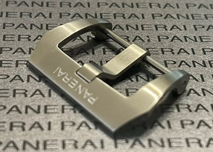 A silver buckle featuring the word "Panerai" displayed on a wooden table.